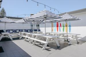 Un grupo de mesas de picnic blancas con sombrillas. en The Surf House, en Byron Bay