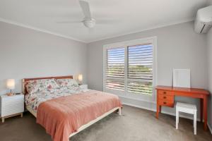 a bedroom with a bed and a desk and a window at Bren Place, 6, Battery Hill in Caloundra