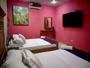 two beds in a room with pink walls and a tv at Hotel Gues in La Guaca