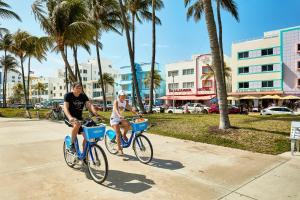 two people riding bikes down a sidewalk with palm trees at Rock Apartments by Lowkl in Miami Beach