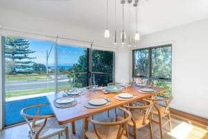 a dining room with a table and chairs and windows at Softlanding in Mollymook
