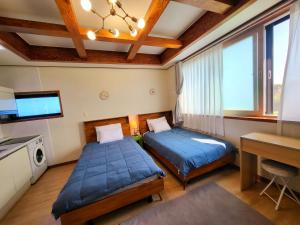 two beds in a room with a desk and window at There Bengdi in Jeju