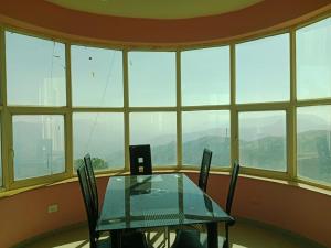 a table and chairs in a room with windows at Dev anand Villa in Mahabaleshwar