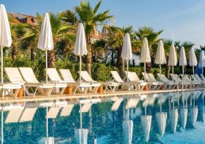 a row of white chairs and umbrellas next to a swimming pool at Armas Life Belek in Belek