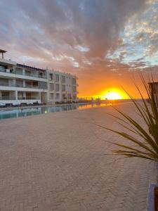 a sunset at the beach with buildings and a plant at Appartement Vue Mer piscine olympique in Aourir