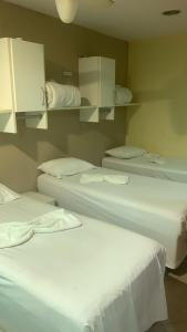 three beds in a room with white sheets at Suítes felicidade Rio Centro in Rio de Janeiro