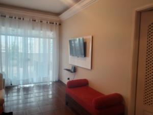 een woonkamer met een rode bank en een flatscreen-tv bij Cobertura com churrasqueira São Vicente in São Vicente
