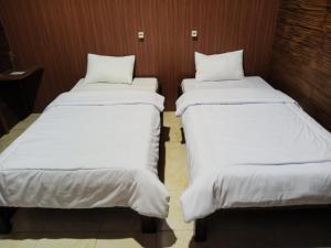 two beds in a room with white sheets at Indah Damai Cottages in Sidomukti