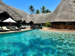 a resort swimming pool with chairs and a thatched roof at Blue Bay Village in Watamu
