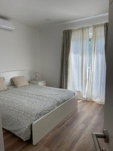 a white bedroom with a bed and a window at Apartamento Tronqueiras in Praia da Vitória