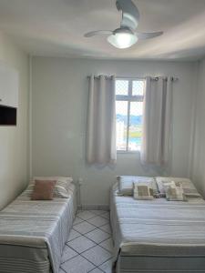 two beds in a room with a window at KITNET ACONCHEGANTE A 3 MINUTOS DA PRAIA in Guarapari