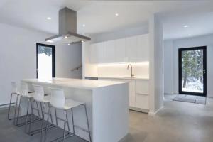 a white kitchen with a counter and stools at Villa Boreale - Wellness and relaxation in Petite-Rivière-Saint-François +45 photos