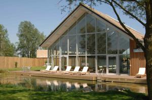 una casa de cristal con sillas blancas y un estanque en Merlin House at Lower Mill Estate A gorgeous home with lake access, air conditioning and luxury spa access, en Somerford Keynes