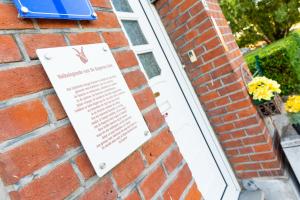 a sign on the side of a brick building with flowers at De Koperen Geit in Kanne