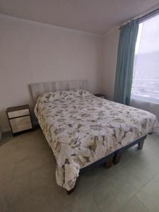 a bed in a bedroom with a window and a bedspread at Departamento Iquique edificio life in Iquique
