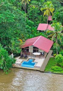 uma casa com um telhado vermelho ao lado de um rio em Valverde Glamping & Ecolodge em Tortuguero