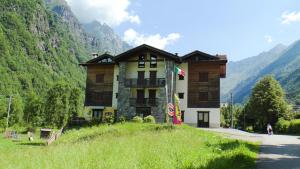 a large building on a hill with mountains in the background at Casa Corti Ostello Ristorante in Valbondione