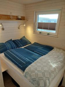 a bed with blue sheets in a room with a window at Hausboot Hecht mit Dachterrasse in Marina Minde, Dänemark in Egernsund