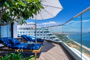 a balcony with blue chairs and an umbrella and the ocean at Mandala Cham Bay Hotel Mũi Né in Mui Ne