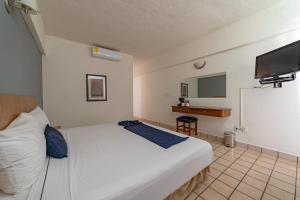 a bedroom with a white bed and a flat screen tv at AM Amakal Hotel & Park in Santa Cruz Huatulco