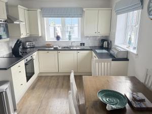 a kitchen with white cabinets and a wooden table at New England Cottage - Part of the The Bay Filey Holiday Village with pool, gym and direct beach access, pub, restaurant, tennis and meadows walks in Filey +46 photos