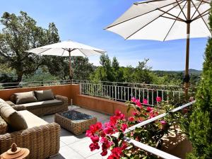 a patio with a couch and an umbrella and flowers at Villa Azur climatisée pour 6 personnes avec piscine et belle vue mer à La Londe les Maures in La Londe-les-Maures