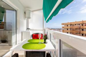 Un balcón con una mesa con cojines verdes y copas de vino. en 523 central Playa las Americas , Wi Fi Gratis y Piscina, en Csta Adje