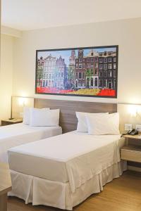two beds in a hotel room with a painting on the wall at Hotel Amsterdam Montes Claros in Montes Claros