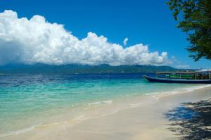 a boat sitting on a beach next to the ocean at BackDoorz Bungalow in Gili Trawangan