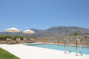 a swimming pool with chairs and umbrellas next to a wall at Pelagia's Loft Villas Haroupi & Rodi with Private Heated Pools, 5 Walking Distance to the Beach in Kavros