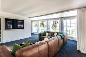 sala de estar con sofá marrón y ventanas en Lannan Beach House - Stay Waiheke, en Waiheke Island