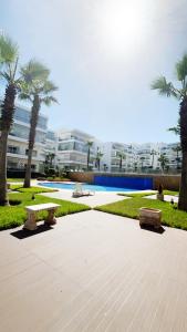 a park with benches and palm trees and a building at Seaside studio with pool in Dar Bouazza