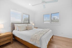 a white bedroom with a bed and two windows at Banksia Breeze Villa - 100m to North One Mile Beach in Forster
