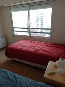 Un dormitorio con una cama roja y una gran ventana. en Deptomarmdp, en Mar del Plata