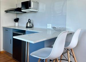 a kitchen with two white chairs at a counter at Casa Sí Apartment in Gqeberha
