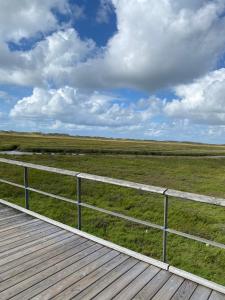 a wooden boardwalk leading into a field with a fence at Ferienwohnung "Seewind" direkt an der Nordsee in Sankt Peter-Ording +5 photos