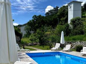 a swimming pool with white chairs and umbrellas at Luxury Lovran Apartments with Swimming Pool in Lovran