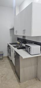Una cocina con gabinetes blancos, un fregadero y un microondas. en Habitaciones Chueca, en Madrid