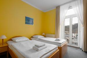 two beds in a room with yellow walls and a window at Wellness Hotel Jean De Carro in Karlovy Vary