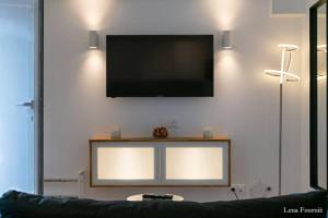 a flat screen tv on a wall with a couch at Maison chaleureuse jacuzzi PS2-1, climatisation et parking payants in Bagneux