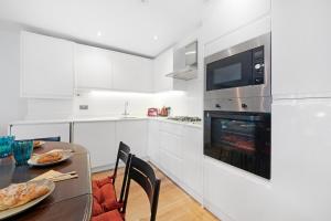 a white kitchen with a table and a fireplace at Hermitage Road Apartment By Morethanstays in London