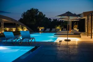 a pool with chairs and an umbrella at night at Nestor Luxury Villas in Romanu