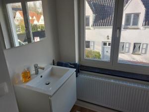 a white bathroom with a sink and two windows at Domein 15 De Haan Nieuwmunster, 4-bedroom holiday house for up to 6 people, between Wenduine, 1 km, and De Haan, 2 km, 500 meters from the beach,15 min from Bruges, Ostend and Knokke, nice fenced garden, no services offered in Zuienkerke +35 photos