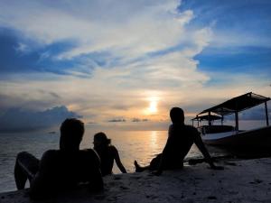a group of people sitting on the beach watching the sunset at Ayu Hotel Karimunjawa in Karimunjawa