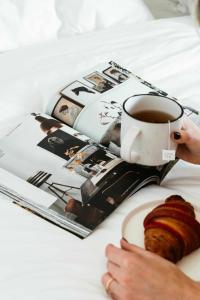 a person holding a cup of coffee and a pastry and a magazine at Benambra Cottage c1860 in Queenscliff
