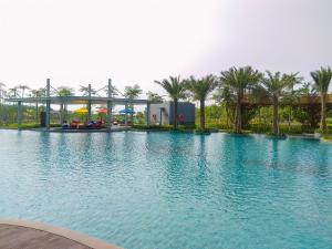 a large swimming pool with palm trees and a bridge at Modern Look and Warm 1BR at Gold Coast Apartment By Travelio in Jakarta