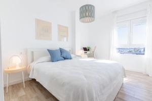 a white bedroom with a large white bed with blue pillows at Balcón Mediterráneo - Desconexión a pie de playa in Santa Pola