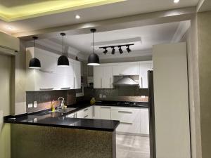 Una cocina con gabinetes blancos y encimeras negras. en New Cairo Hotel Apartment, en Madīnat ash Shurūq
