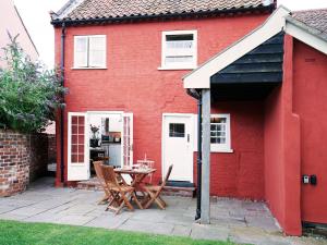 a red house with a table and chairs on a patio at Hidden Cottage by The Suffolk Cottage Collection in Aldeburgh