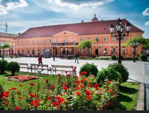 ein großes Gebäude mit einem Park mit Bänken und Blumen in der Unterkunft Nina centar in Sombor